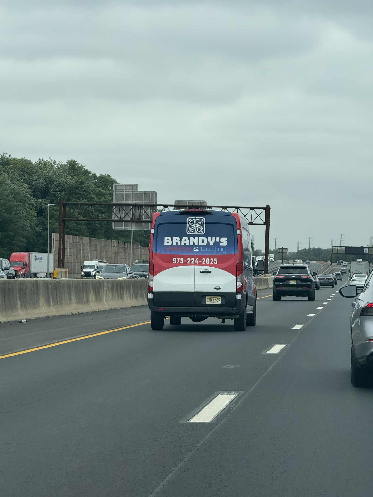 A truck with a red, white, and blue design drives on a highway with other vehicles under a cloudy sky.