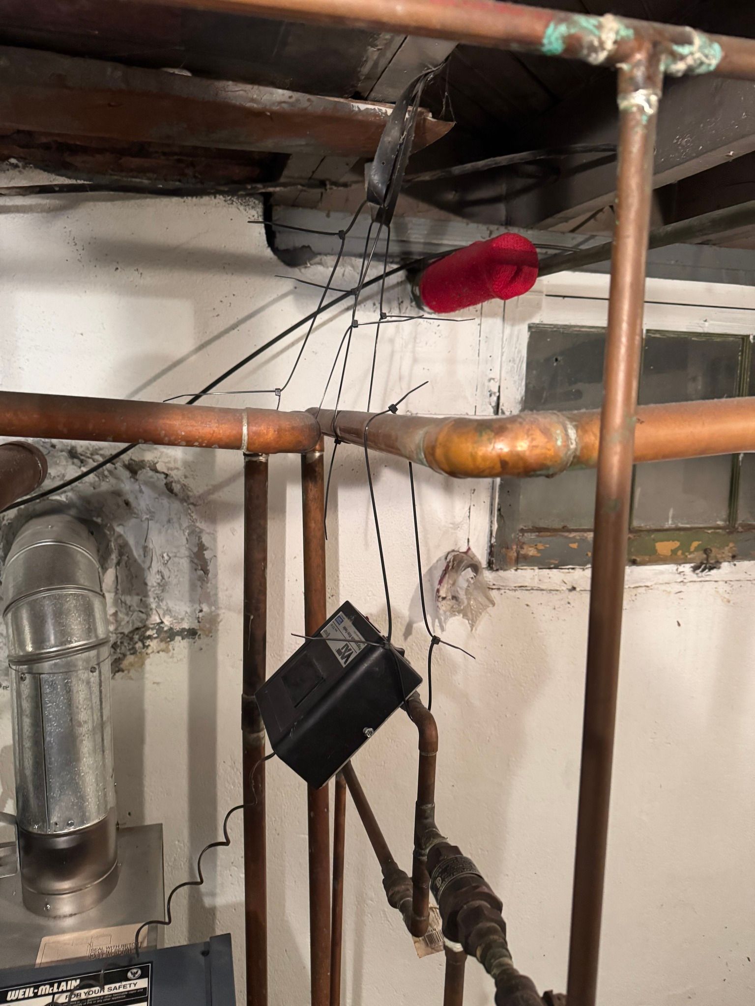 Copper pipes, black object, and vents in a basement.