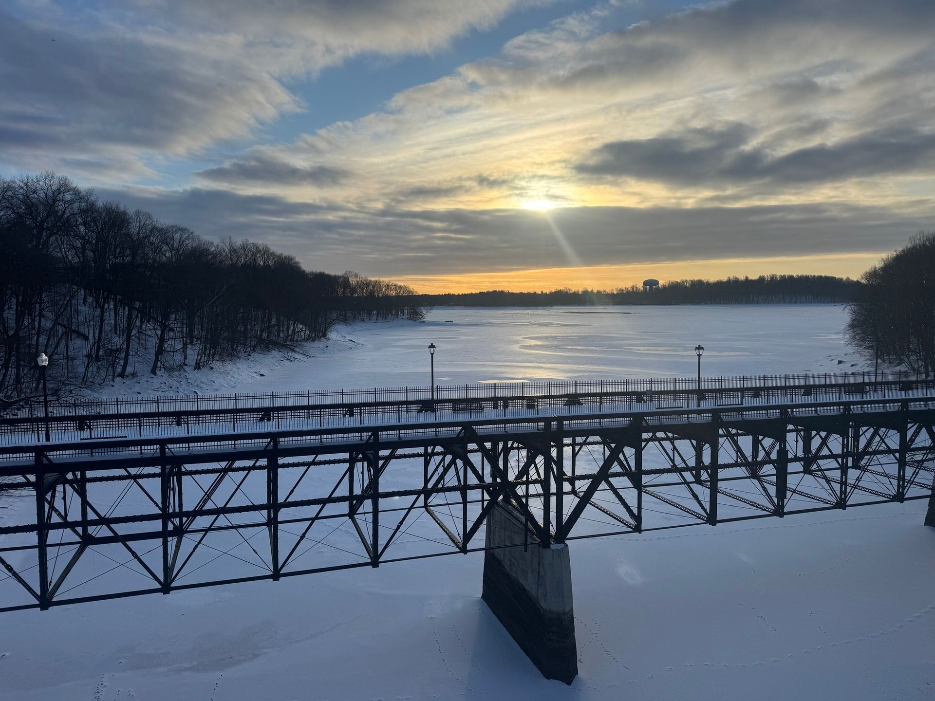 Snowy landscape with bridge over frozen lake at sunset.