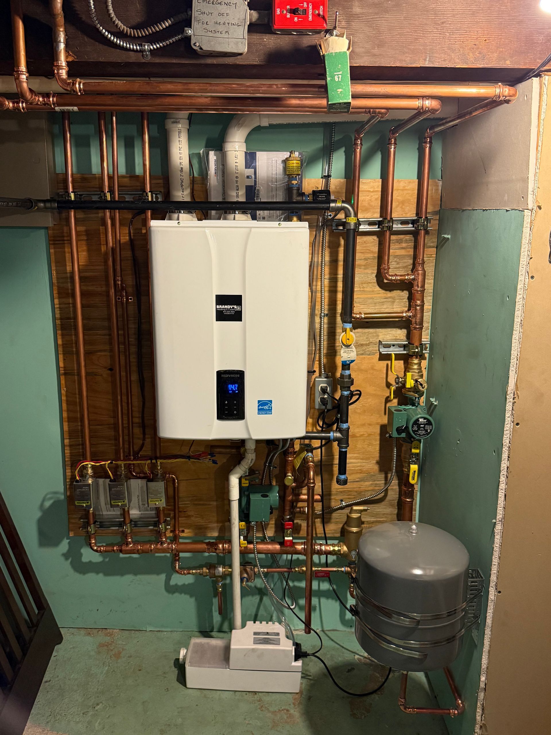 Copper pipes, a white tankless water heater, and related plumbing against a green-painted wall.