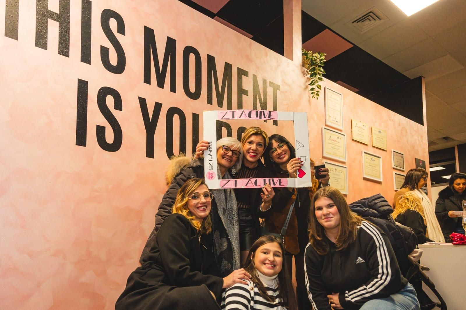 Un gruppo di donne posa per una foto davanti a un muro su cui è scritto ``questo momento è tuo''.