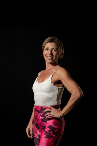 Una donna con una canottiera bianca e leggings rosa è in piedi con le mani sui fianchi.