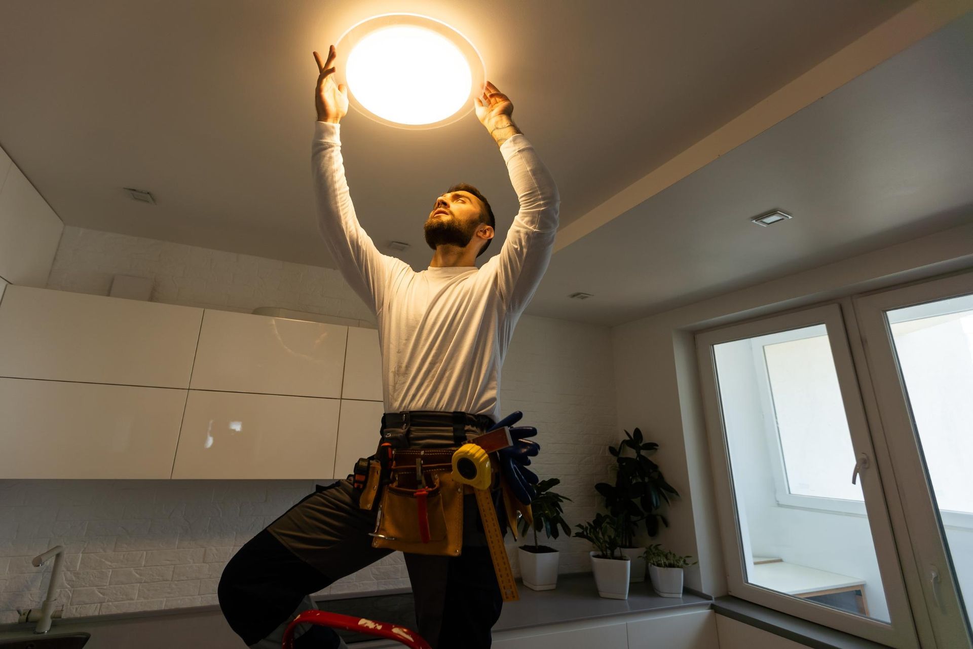 A man is installing a light fixture on the ceiling in a kitchen.