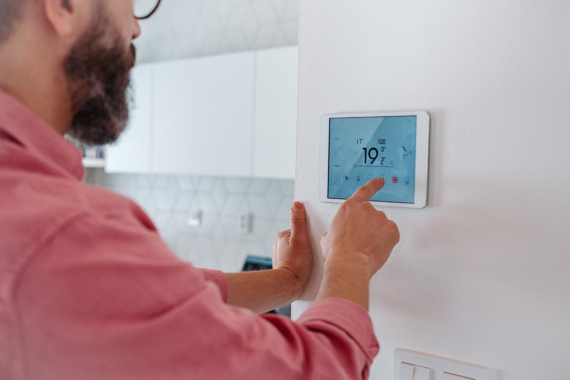 A man is using a smart thermostat on a wall.