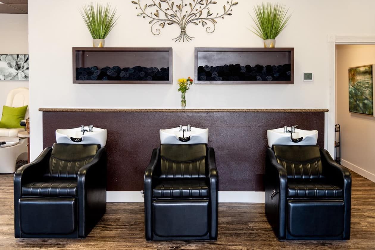 Three black salon chairs with shampoo bowls; interior salon.
