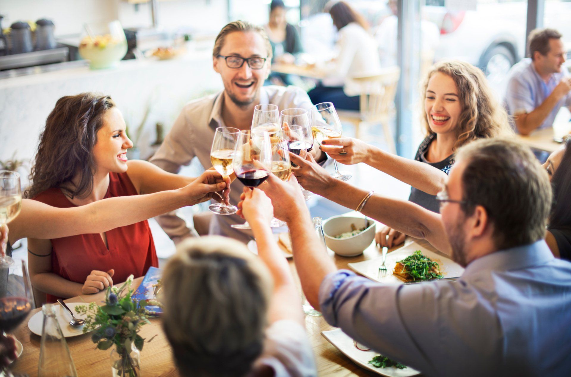 Group of friends toasting with wine at a restaurant table, smiling, cheerful atmosphere.