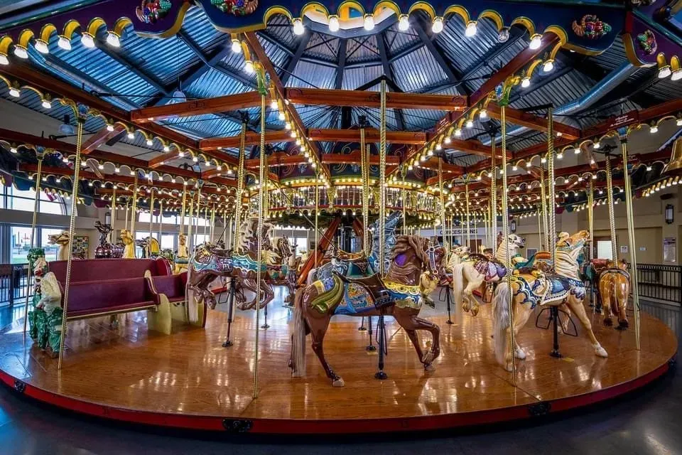 Carousel with carved horses under a domed ceiling, brightly lit, wooden platform.