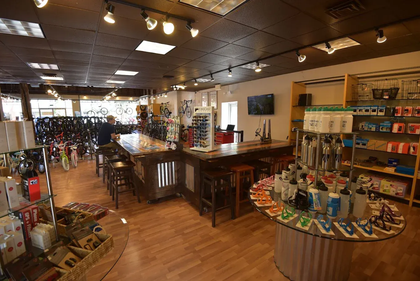 Interior of a bike shop with bicycles, accessories, display tables, and a customer.