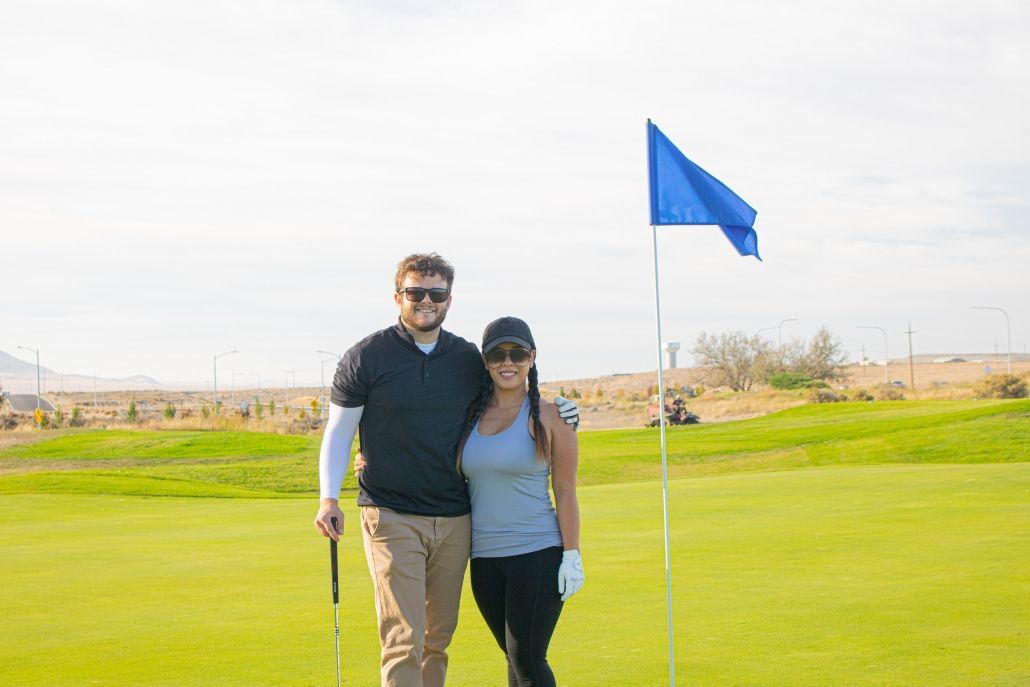 Couple smiling on a golf course, standing by a blue flag.