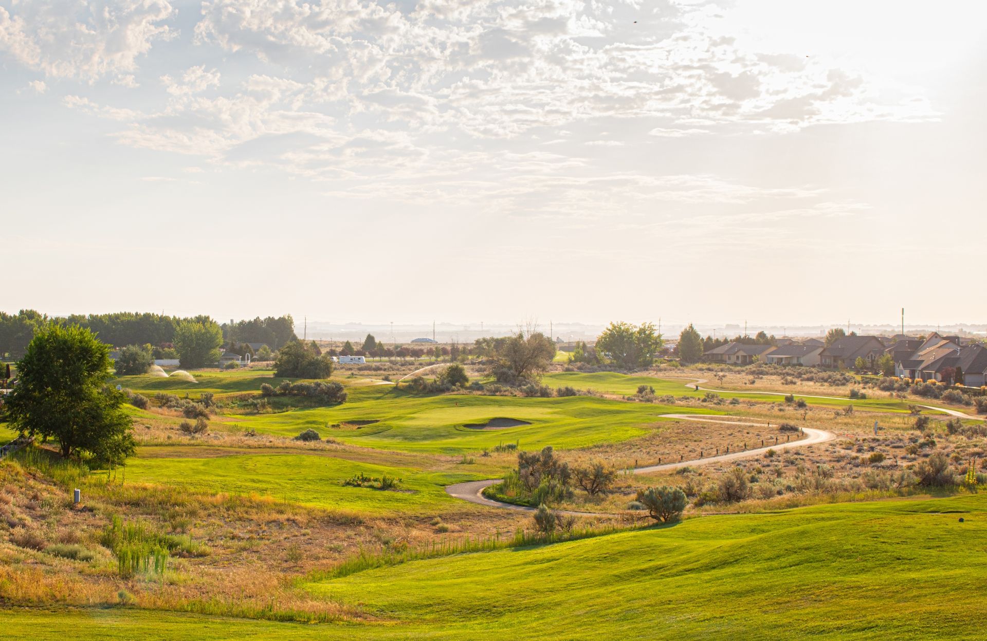 Vast, sunny landscape featuring a golf course, trees, and golden-green grass under a bright sky.