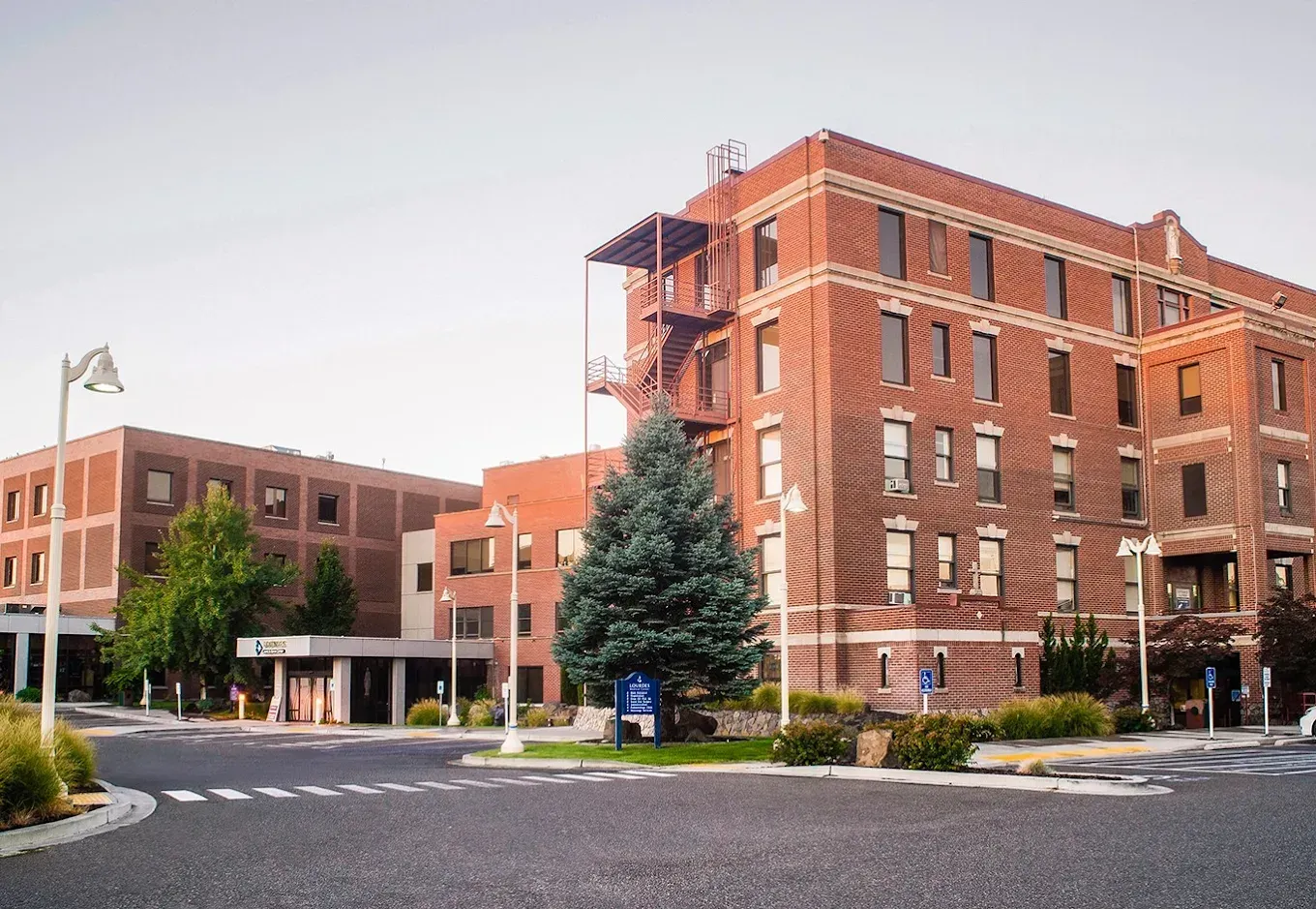 Brick hospital building with multiple stories and a blue sign outside.