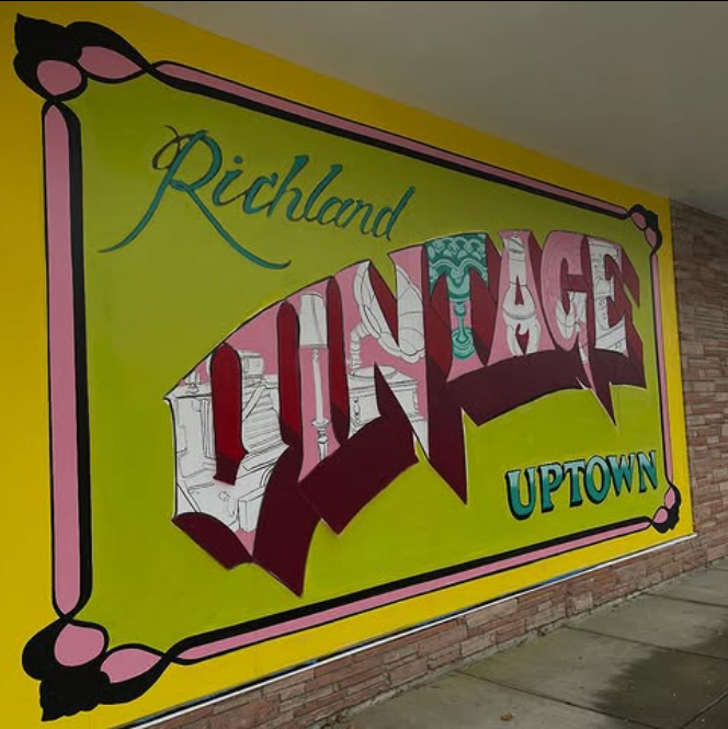 Sign for Richland Vintage Uptown, painted on a yellow wall, with pink and black trim.