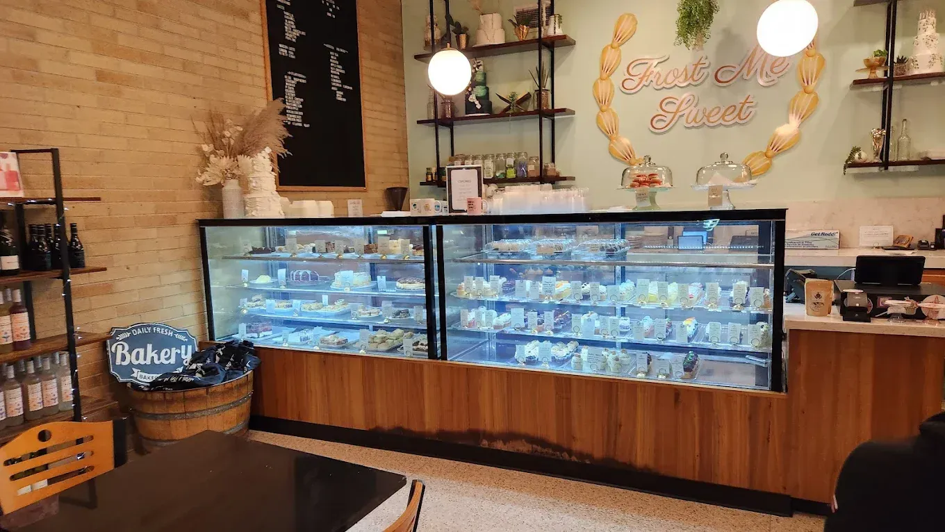 Bakery interior: display case with pastries, shelves, sign, wooden counter, brick wall.