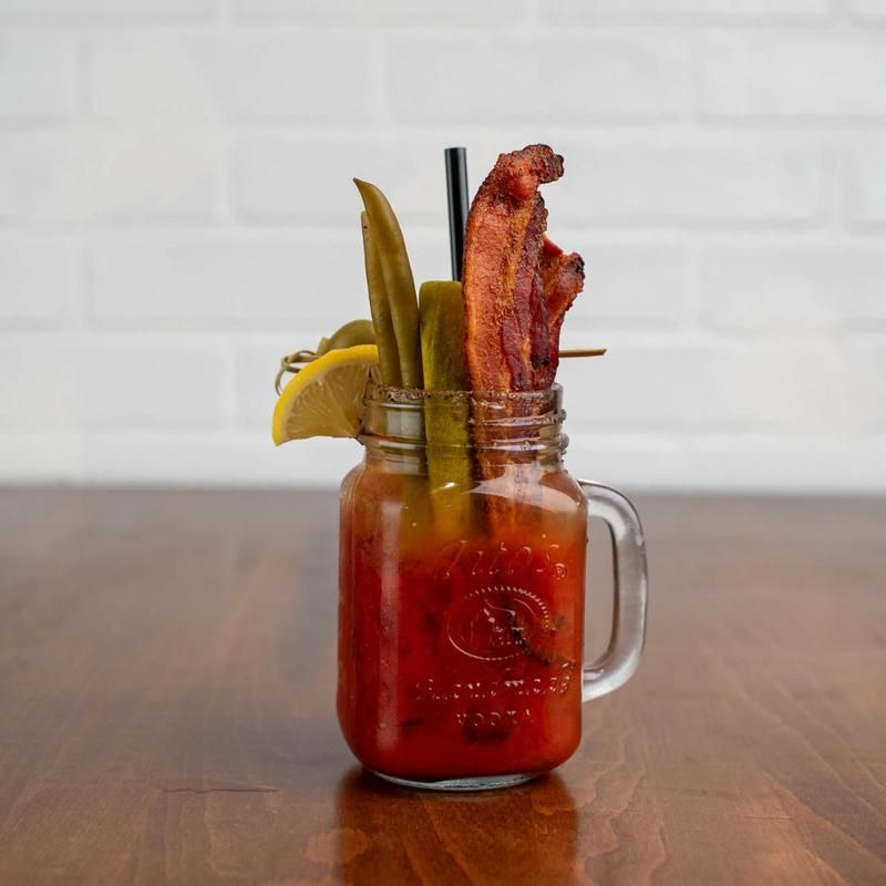 Bloody Mary cocktail in a mason jar, garnished with bacon, pickles, and lemon.