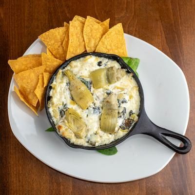 Artichoke dip in cast iron skillet with tortilla chips on a white plate.