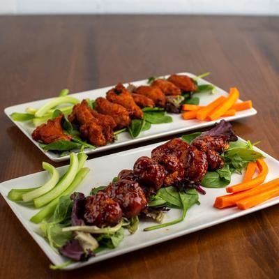 Two plates of chicken wings with vegetables, on a wooden table.