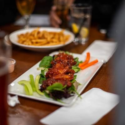 Plate of Buffalo wings with celery and carrots, fries, and drinks on a wooden table.