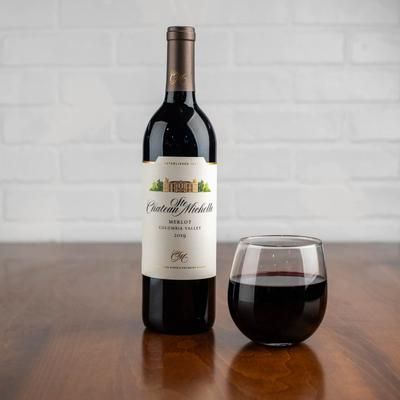 Bottle of red wine and stemless glass on a wooden table. Brick wall background.