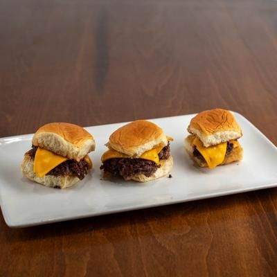 Three cheeseburger sliders on a white rectangular plate, set on a dark wood surface.