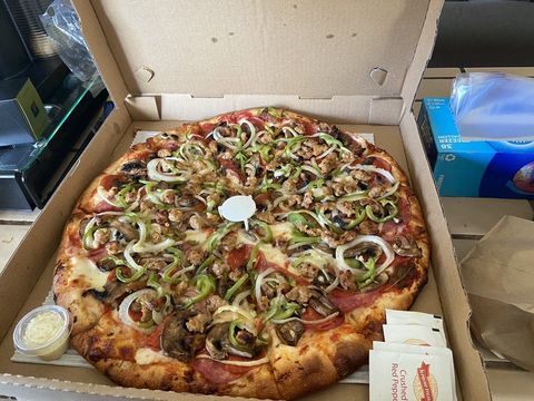 a pizza with a lot of toppings is in a cardboard box .