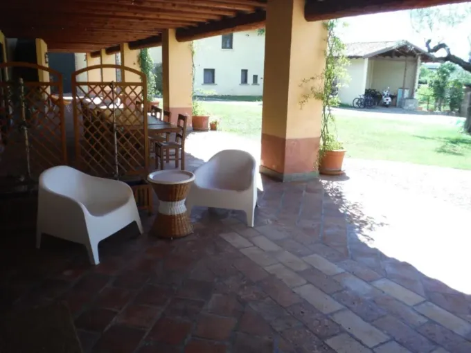 Due sedie bianche e un tavolino su un patio in mattoni sotto un portico, con un prato e un edificio sullo sfondo Villa Antonella