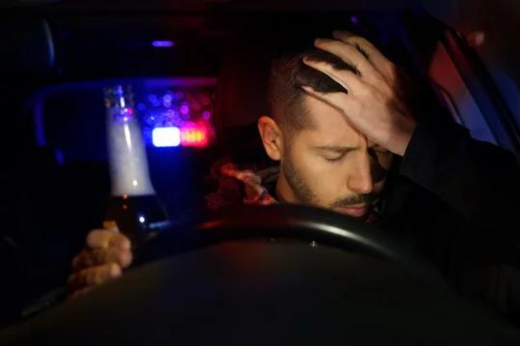 A man is sitting in a car holding a bottle of beer.