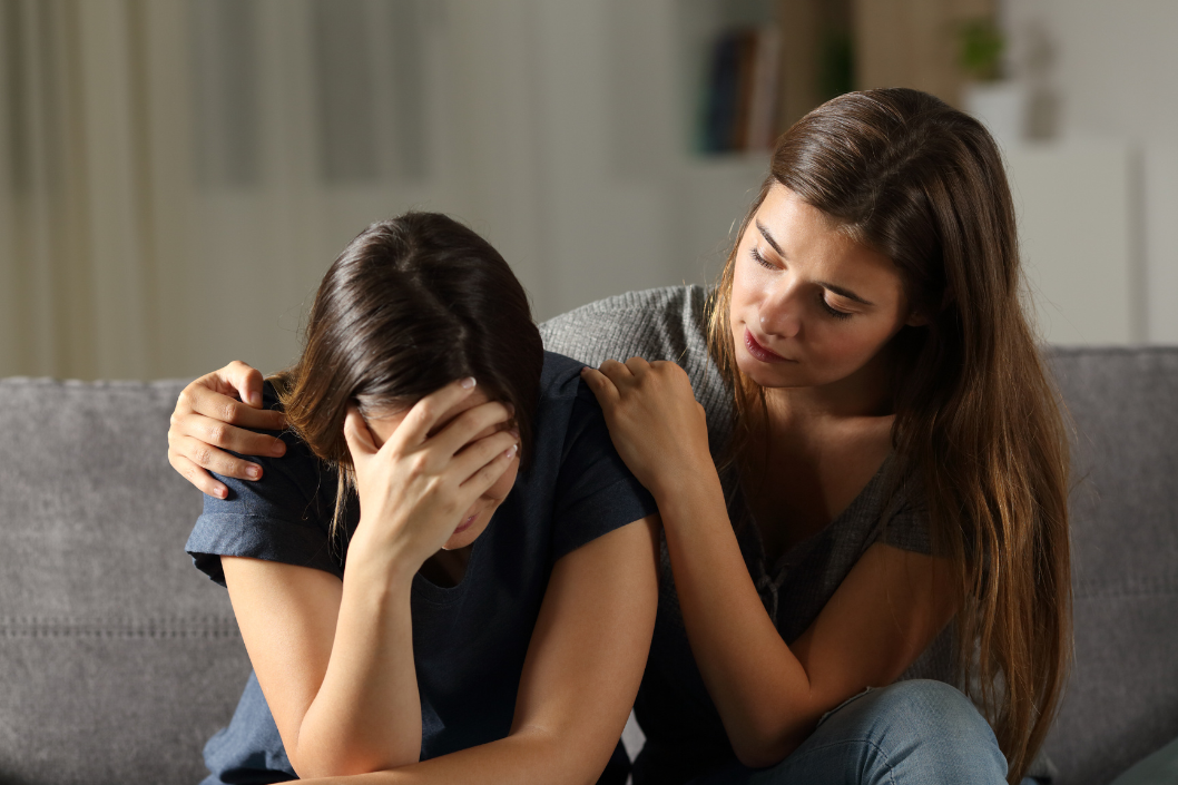 A woman is comforting another woman who is crying on a couch.