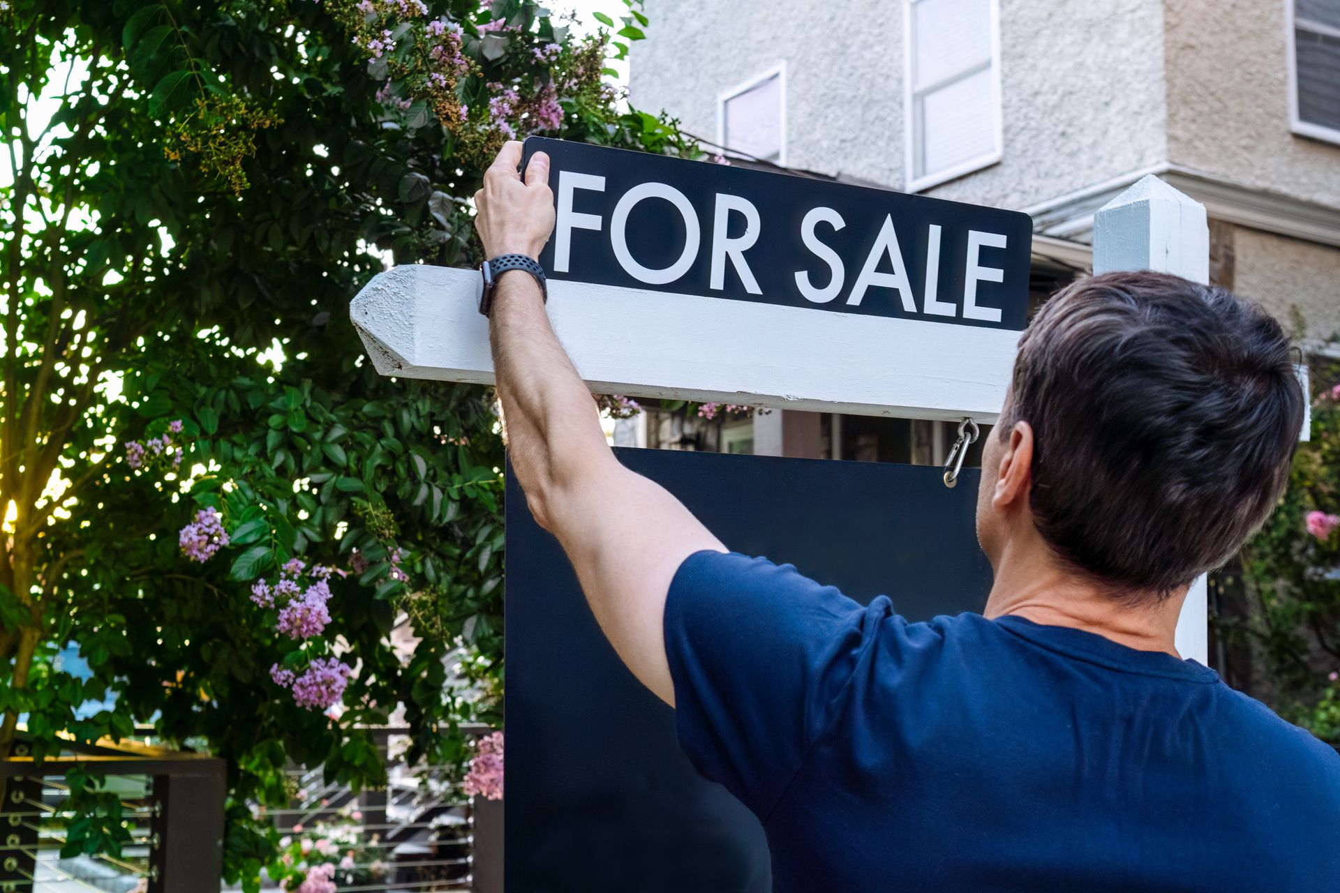 A real estate agent adjusts a for sale sign in a front yard.