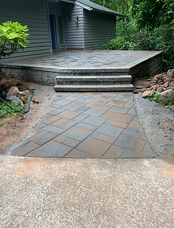 Brick patio with steps leading to a raised deck next to a house with gray siding.