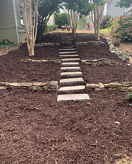 Stone steps lead uphill through a mulched yard with stone retaining walls. Bare trees frame the scene.