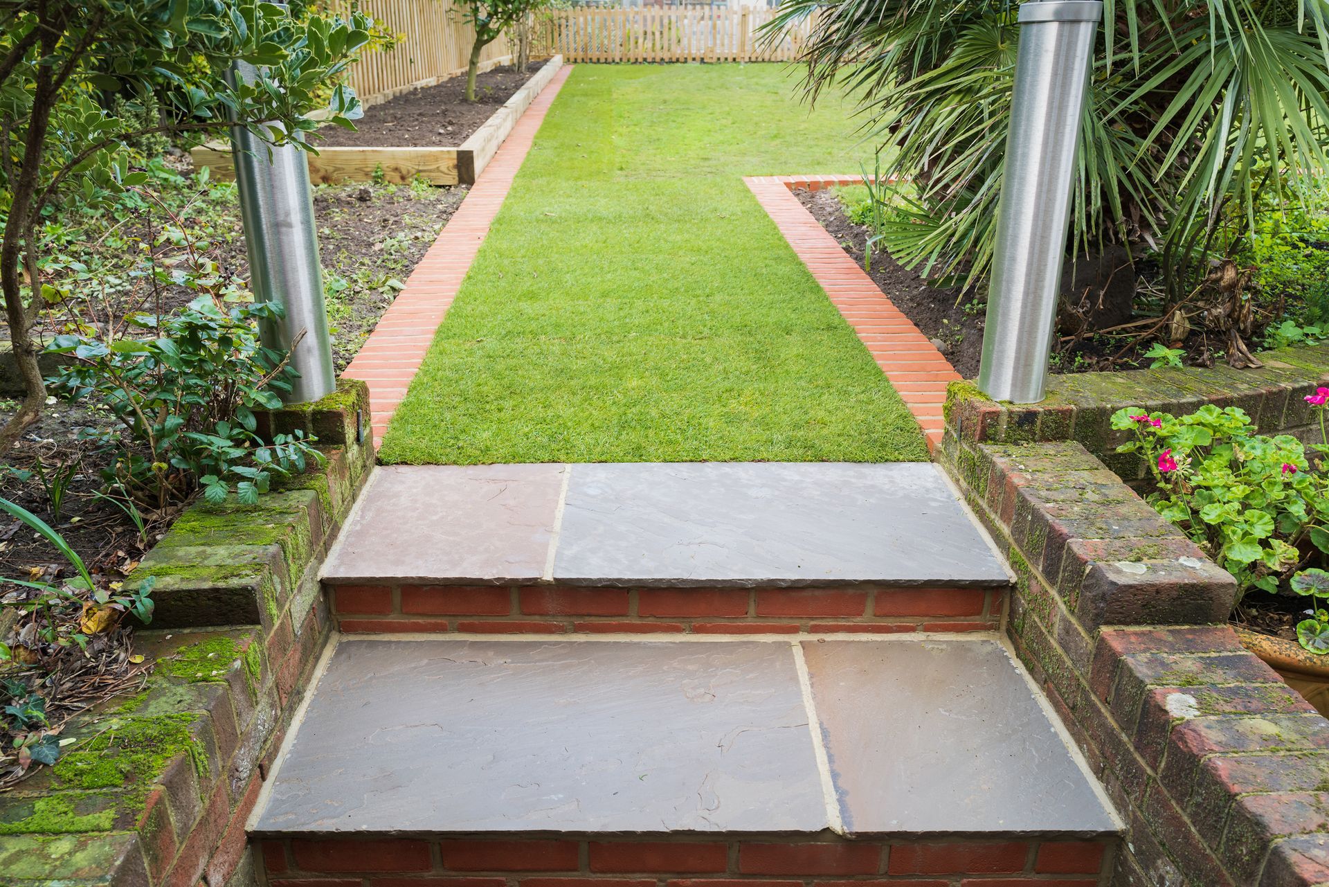 Stone steps leading to a green lawn path bordered by brick and greenery.