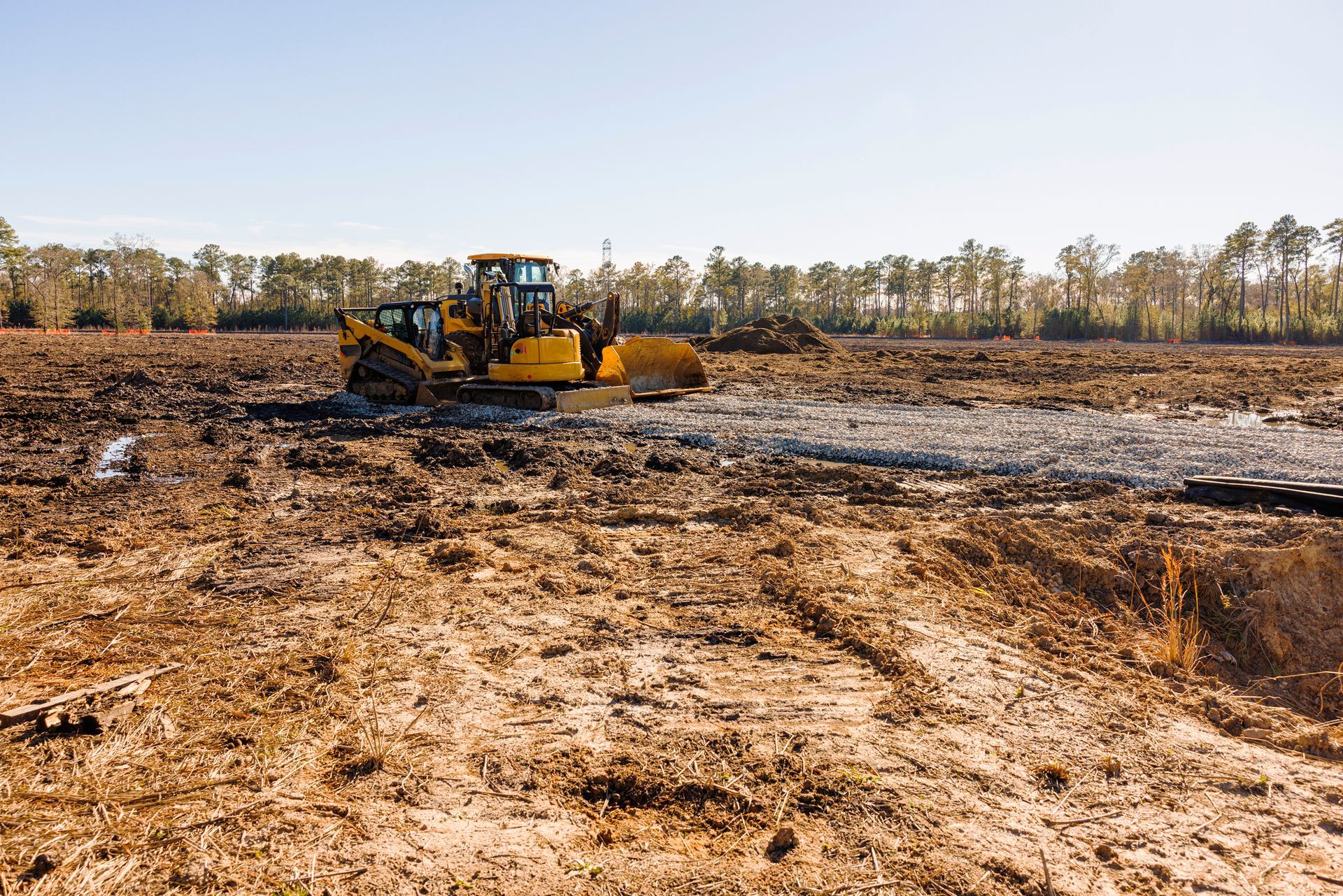 Yellow bulldozer clearing dirt field under a clear blue sky.