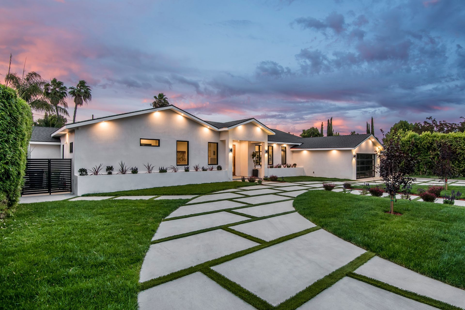 Modern white house with paved driveway on a grassy lawn; dusk sky.