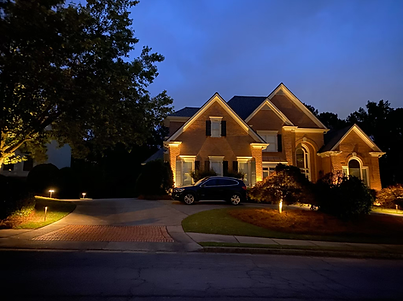 Brick house lit at night, with a car in the driveway and pathway lights.