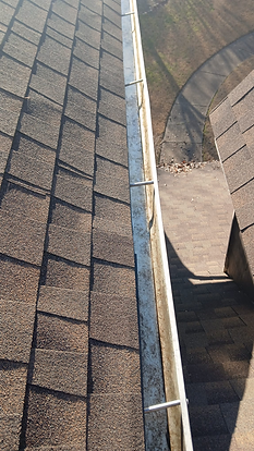 Overhead view of a roof with a gutter. The gutter is metal and dirty.