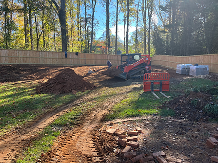 Construction site: Skid steer moving dirt in a backyard, fence in background.