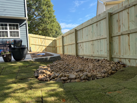 Backyard with newly laid sod, a rock bed, wooden fence, and a blue house.