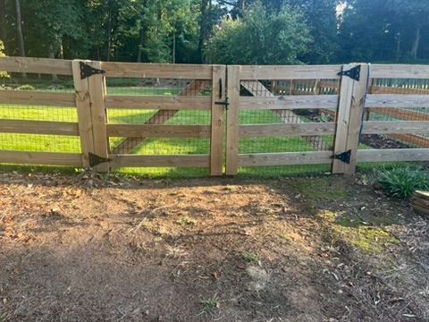 Wooden fence with two gates, surrounded by green grass and trees.
