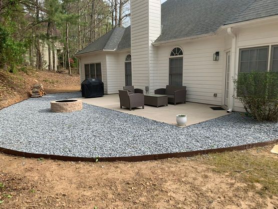 Backyard patio with fire pit, gravel groundcover, and seating next to a white house.