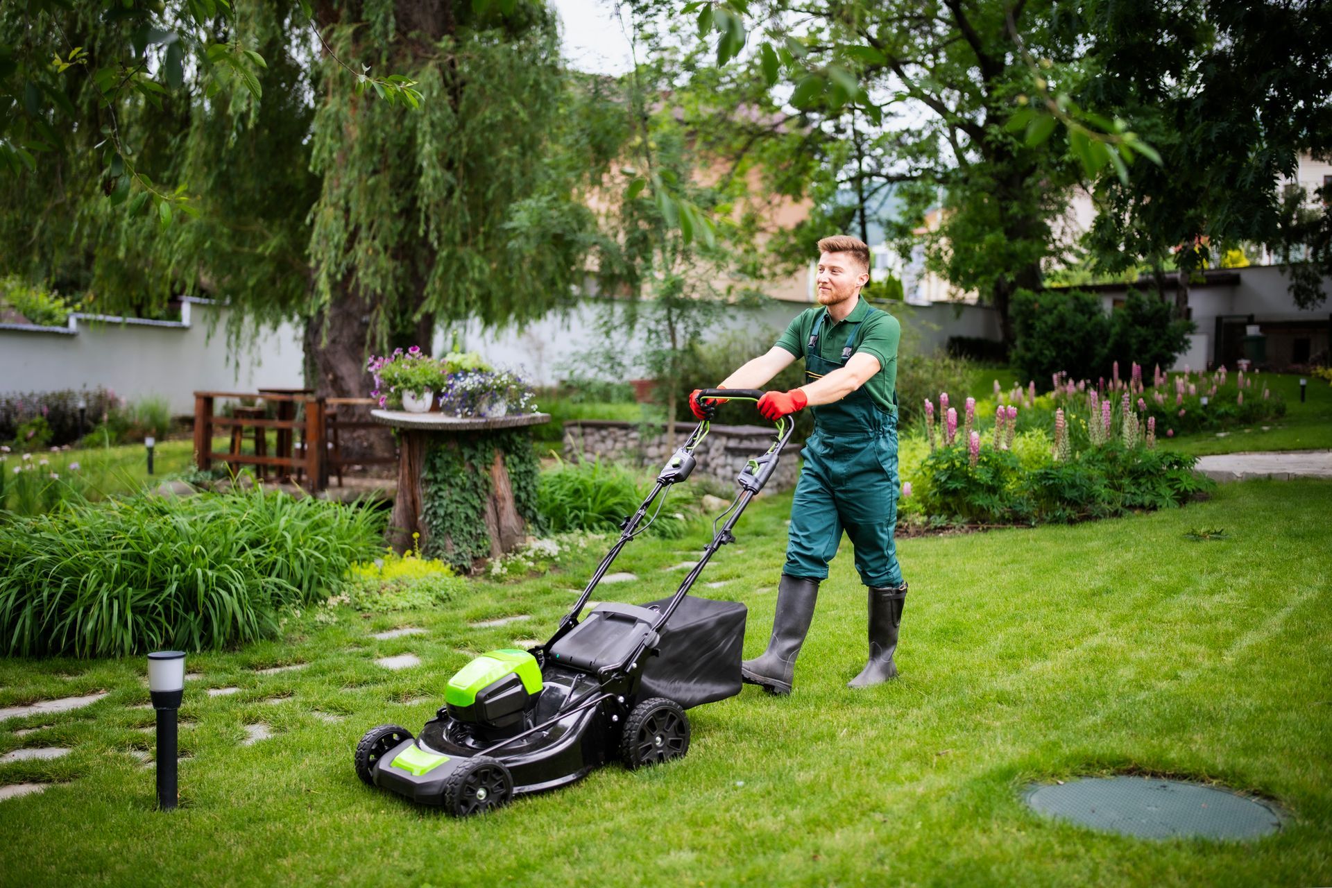 Person mowing a green lawn with a black and green lawnmower in a backyard.