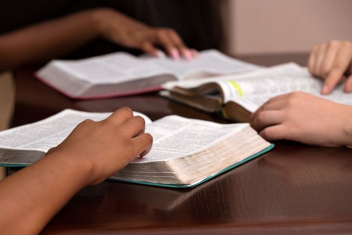 Three people are sitting at a table reading bible