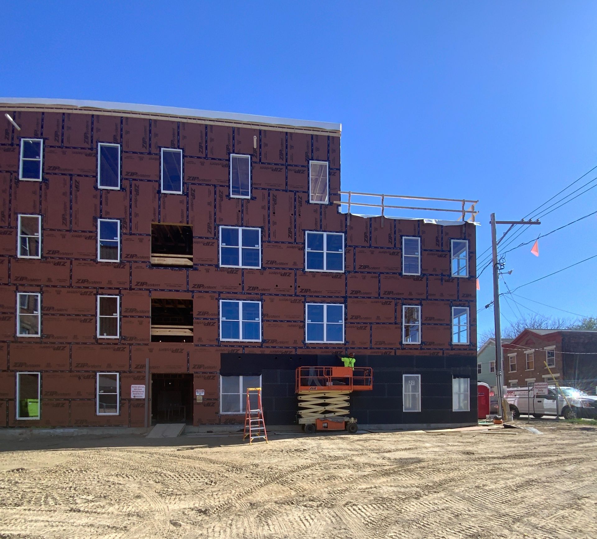 Four-story brick building under construction with scaffolding, windows, and a dirt foreground under blue sky