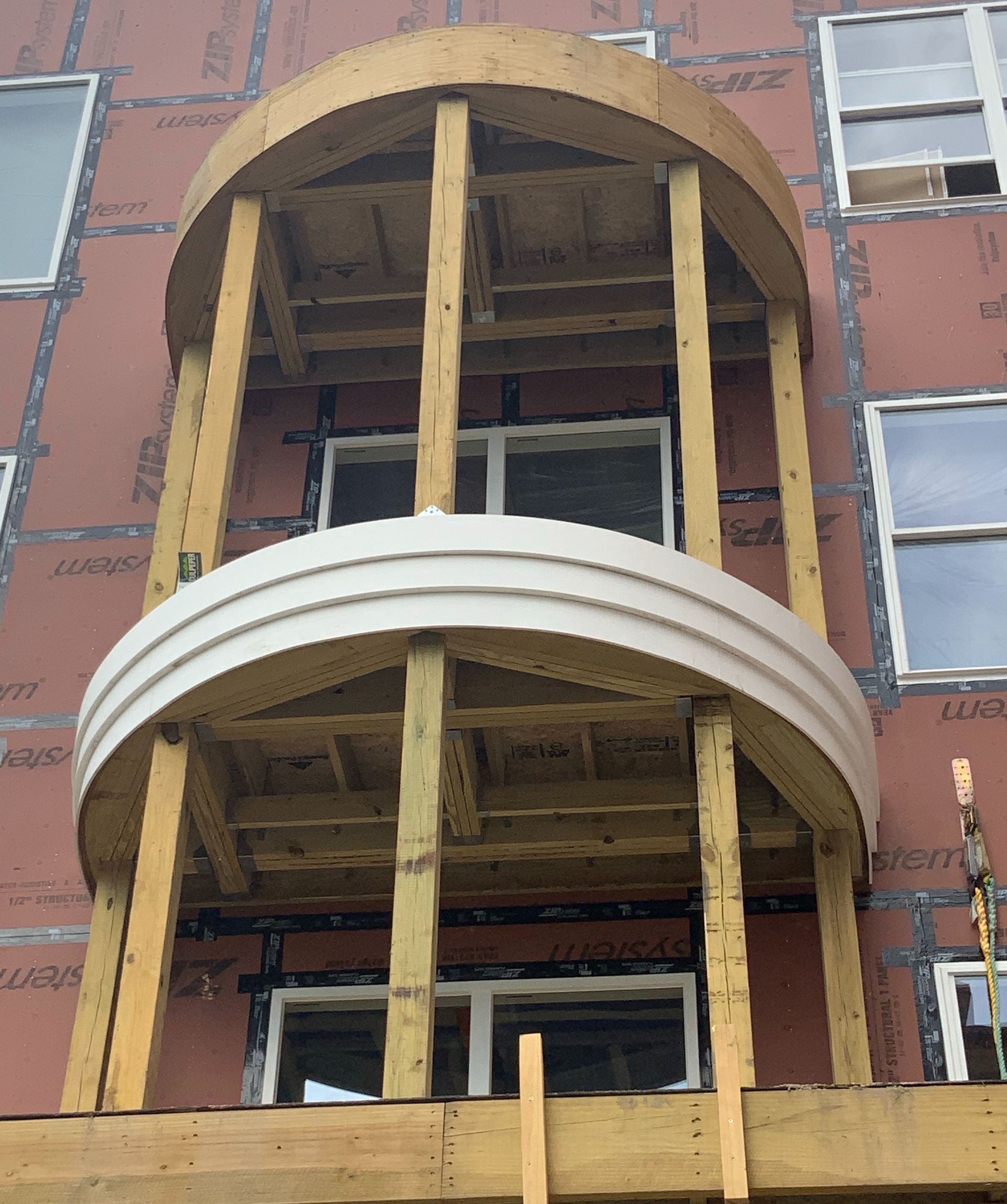 Partially built balcony on a red brick building, with exposed wooden supports and arched openings.