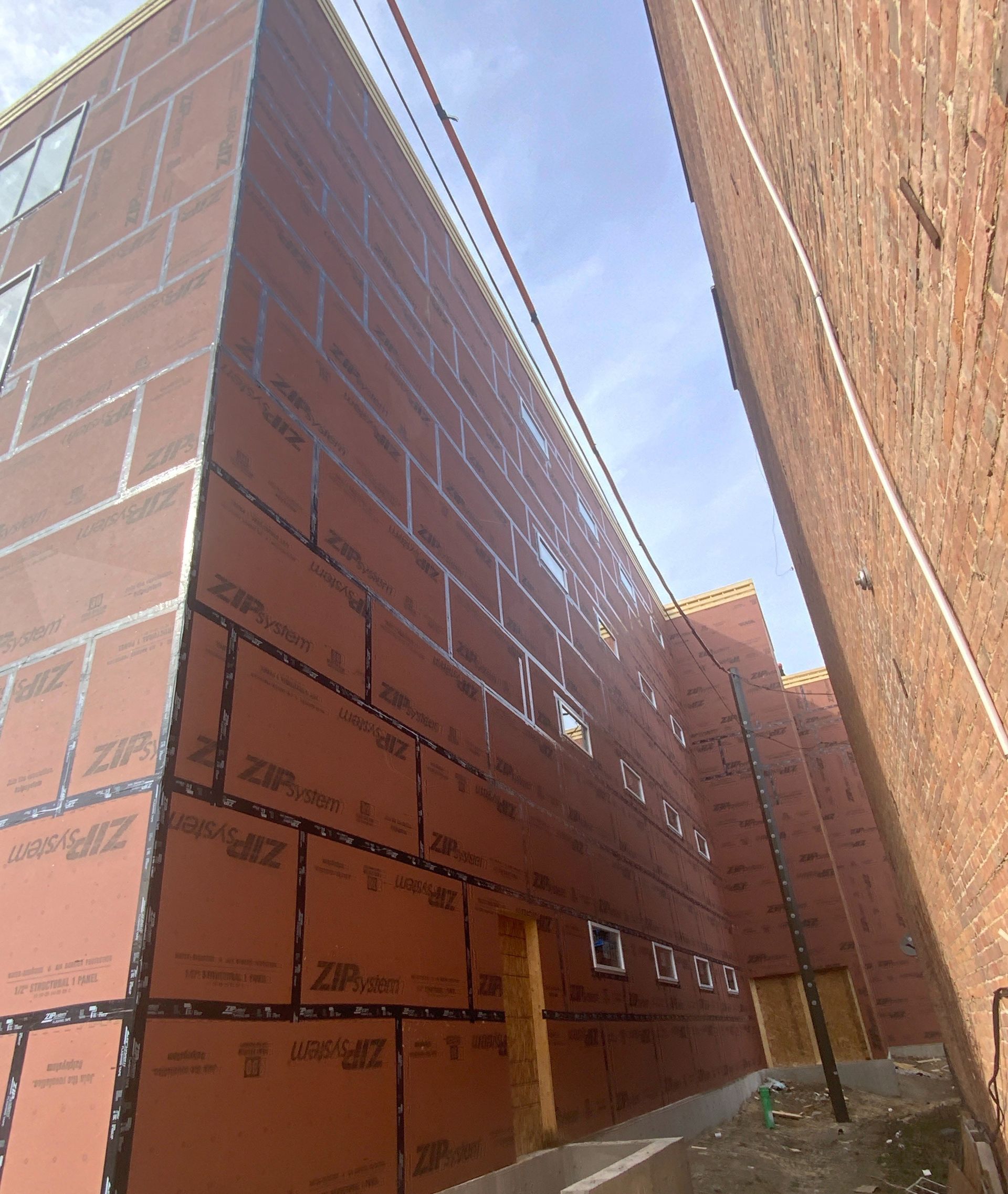 Narrow alley between two brick buildings under construction, with orange insulation boards on the left wall.