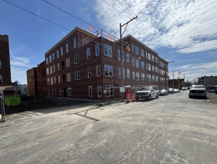 Red brick apartment building on a sunny street with parked cars and utility poles