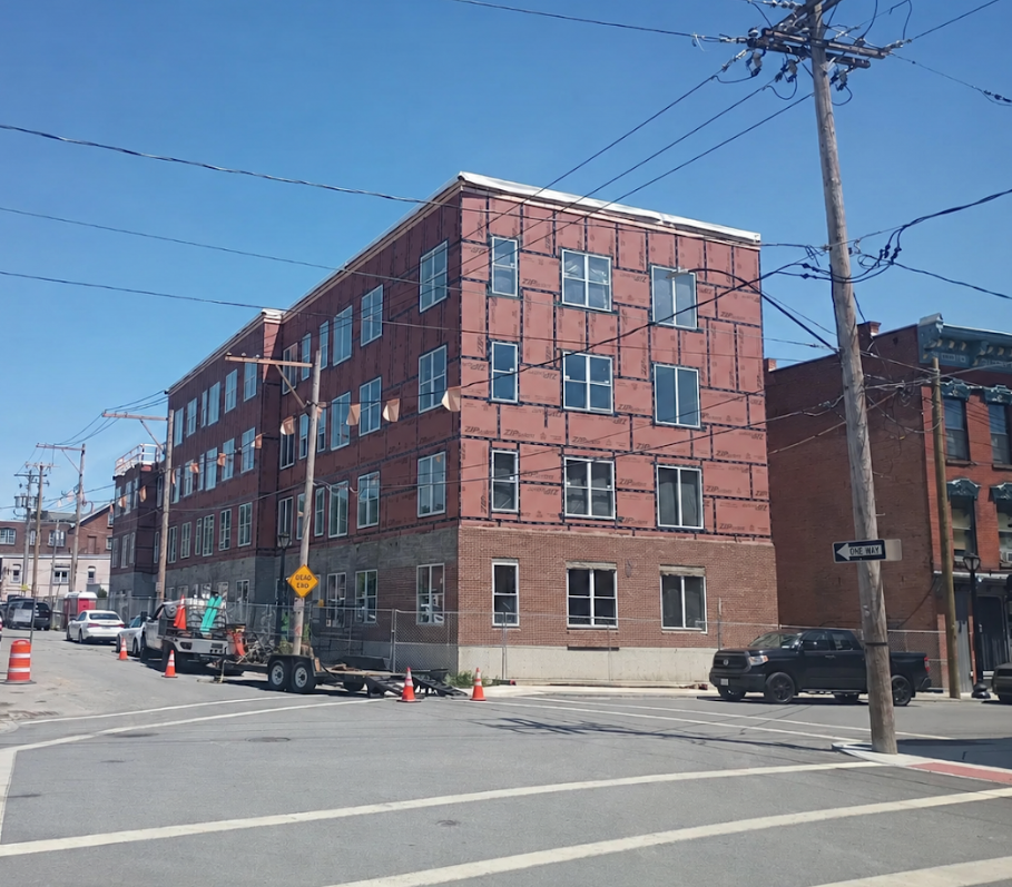 Red brick apartment building on a city street corner with utility poles and parked cars