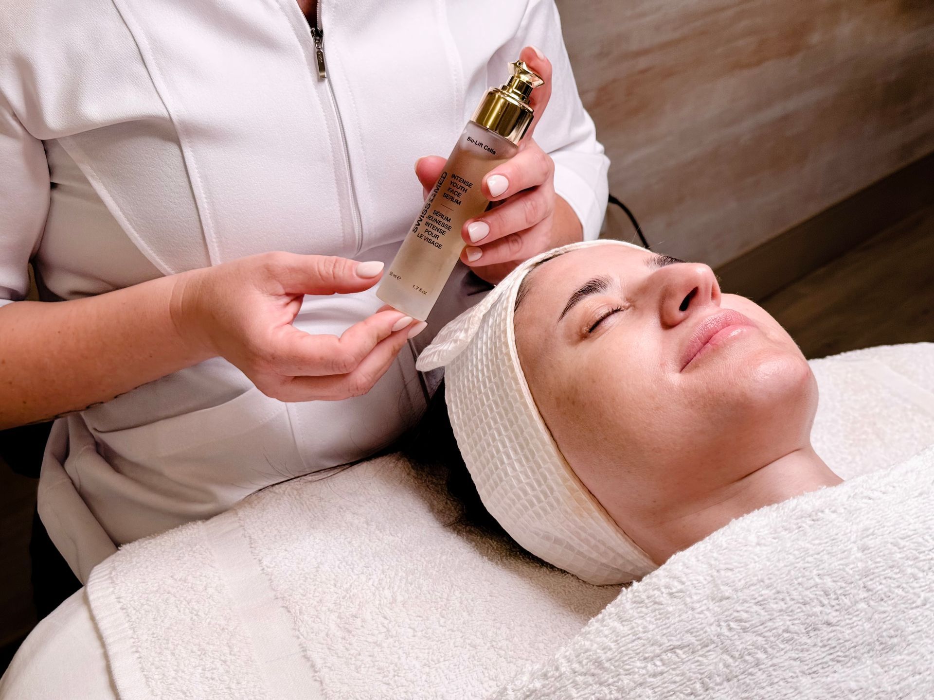 Woman receiving facial treatment, therapist holding skincare product.