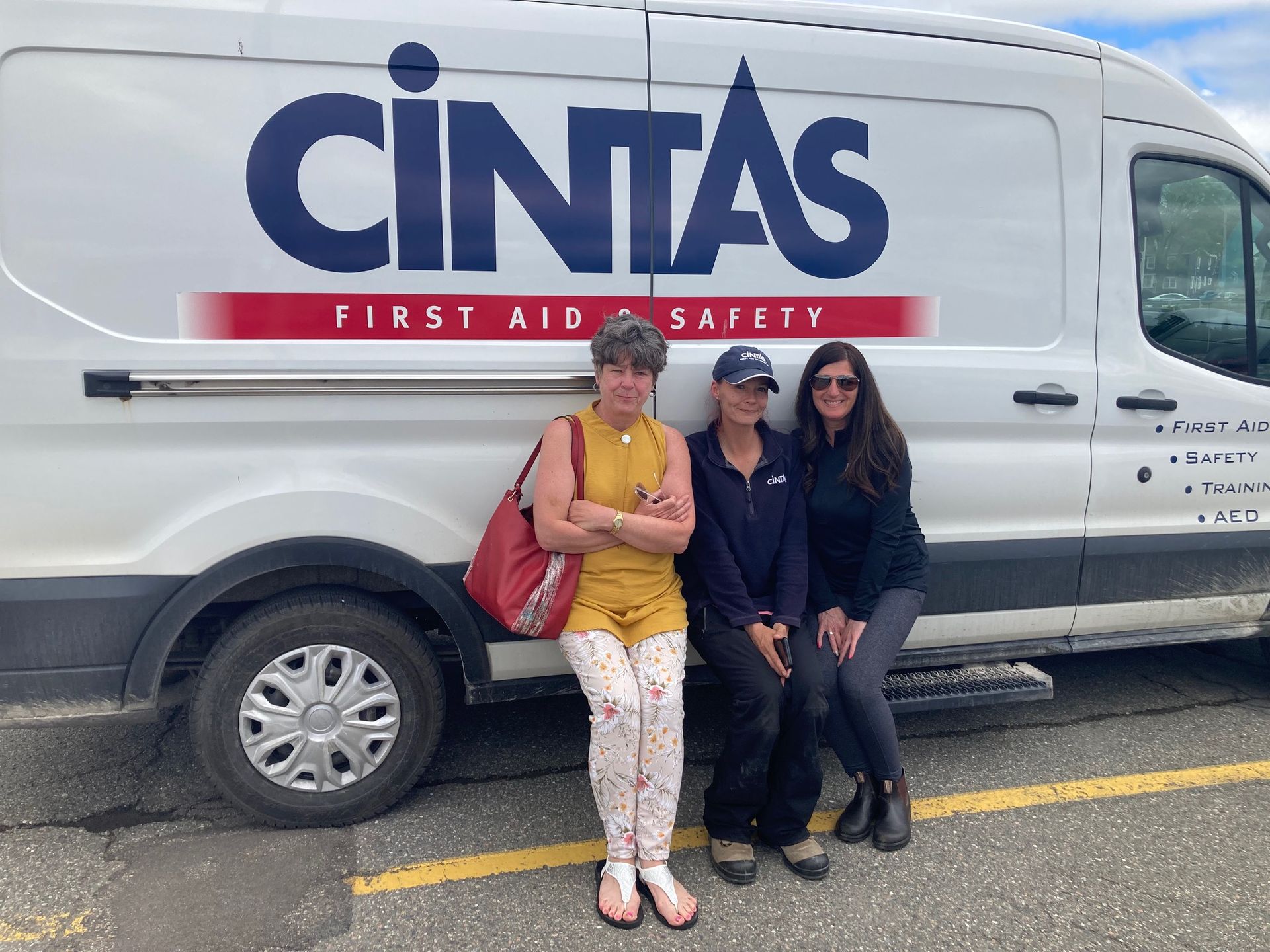 Three women are standing in front of a white cintas van.