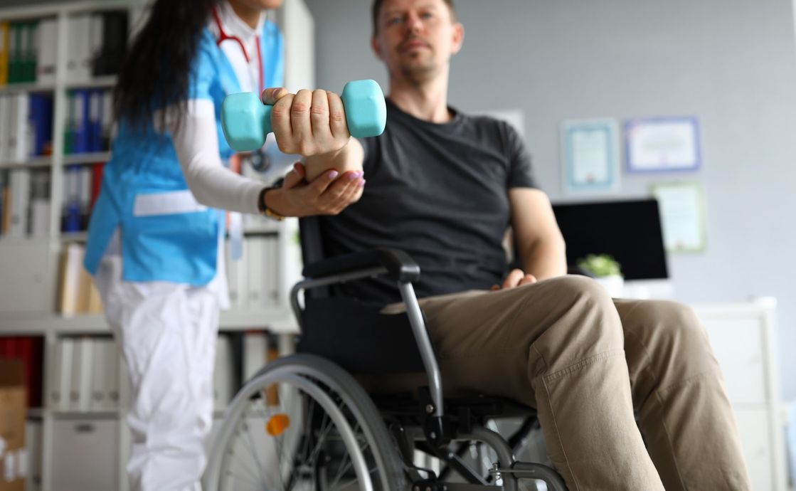A nurse is helping a man in a wheelchair with a dumbbell.