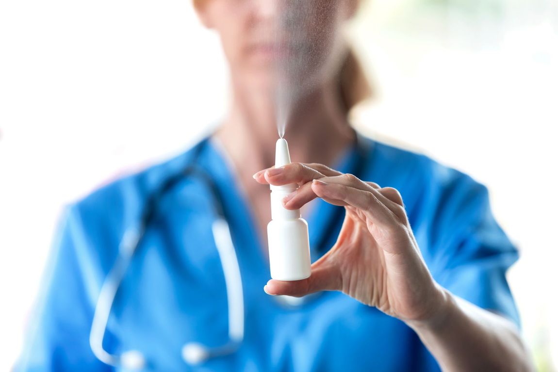 A nurse is holding a bottle of nasal spray in her hand.